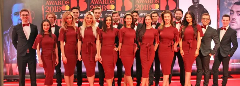 Awards night team of hostesses in red dresses and hosts in black tie on the red carpet