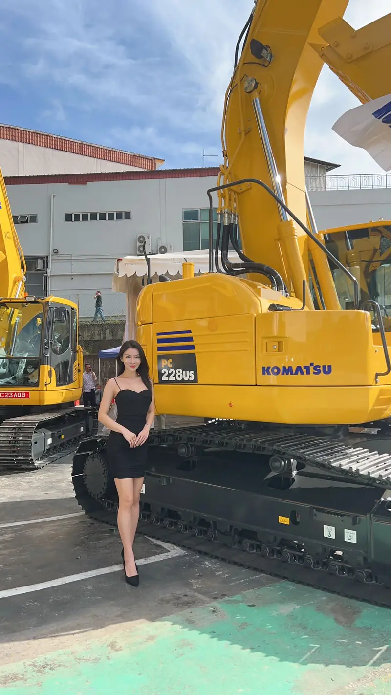 Promotional model beside a new excavator at an outdoor machinery launch