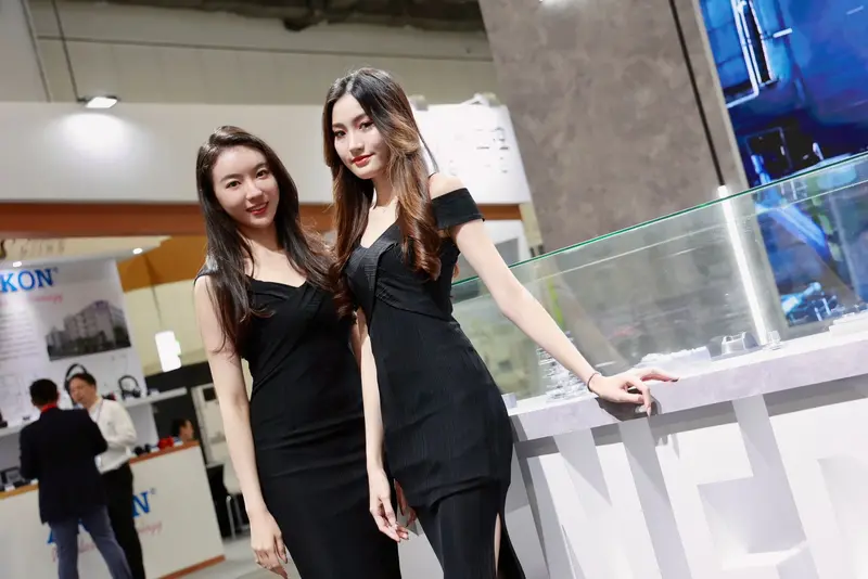 Two exhibition hostesses in black dresses beside a display case on a trade show stand